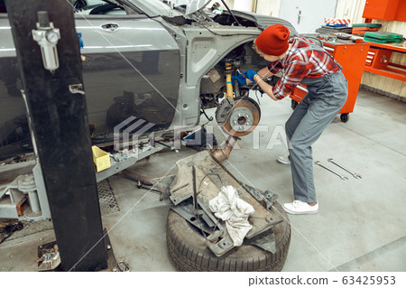 Young female mechanic using an automotive tool Young female mechanic using an automotive tool 63425953