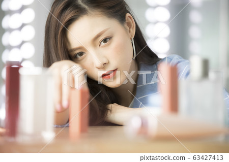 Young woman wearing a jacket with cosmetics placed on a table Young woman wearing a jacket with cosmetics placed on a table 63427413