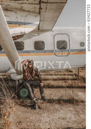 Stylish man is sitting near plane outdoors 63427715