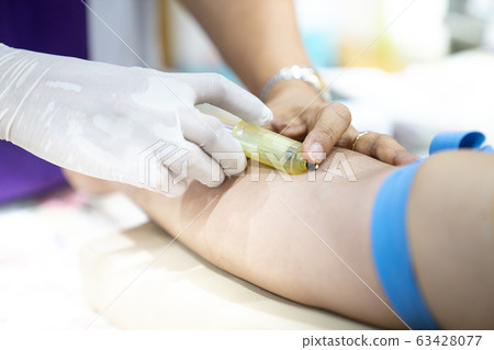 Medical person drawing blood with syringe and hypodermic needle from a patient. 63428077
