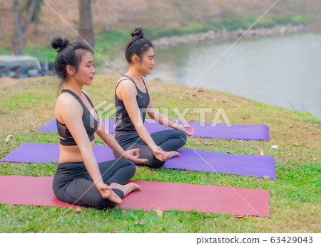 A cute Asian girl is wearing sports clothes sitting in a lotus position while doing yoga. 63429043