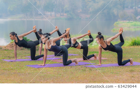 Group of young females practicing yoga the lakeside during the sunrise. 63429044