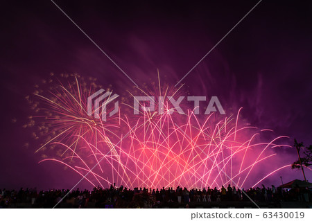 Crowd looks holiday fireworks in dark evening sky. 63430019