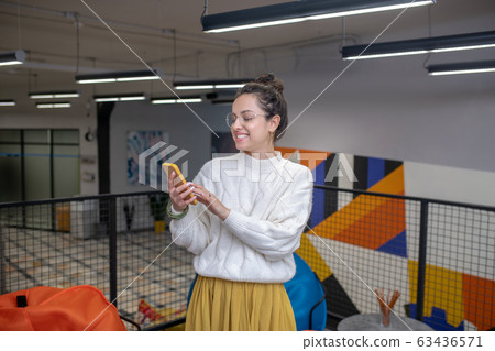 Young woman in eyeglasses, checking her phone, smiling Young woman in eyeglasses, checking her phone, smiling 63436571