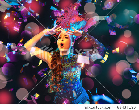 Beautiful young woman in carnival and masquerade costume in colorful neon lights on black background in flying confetti Beautiful young woman in carnival and masquerade costume in colorful neon lights on black background in flying confetti 63437189