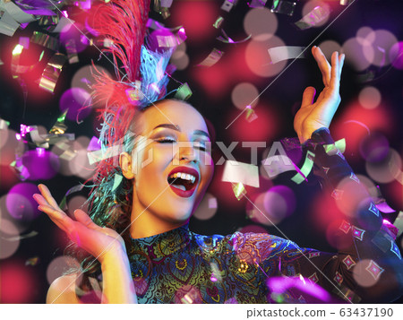 Beautiful young woman in carnival and masquerade costume in colorful neon lights on black background in flying confetti 63437190