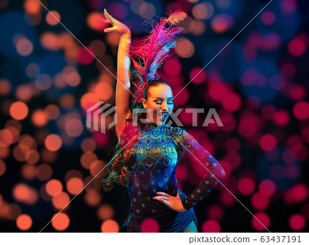 Beautiful young woman in carnival and masquerade costume in colorful neon lights on black background in flying confetti 63437191