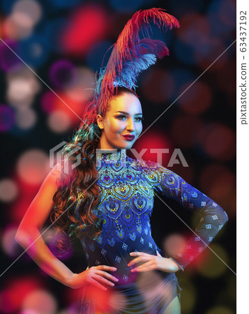 Beautiful young woman in carnival and masquerade costume in colorful neon lights on black background in flying confetti Beautiful young woman in carnival and masquerade costume in colorful neon lights on black background in flying confetti 63437192