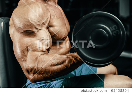 Bodybuilder strong man pumping up biceps muscles 63438294