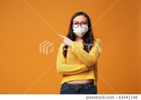 Chine woman with glasses and medical mask pointing hand to side in studio Chine woman with glasses and medical mask pointing hand to side in studio 63441146