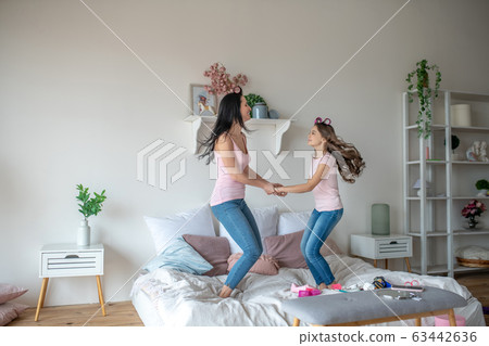 Mom and daughter with hair curlers having fun while jumping on the bed 63442636