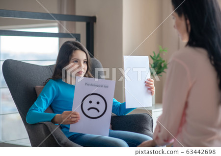 Long-haired teen in a blue shirt holding a table with a sad face 63442698