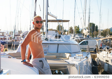 Happy young man feels happy on marina near the luxury sail boat yacht catamaran in summer holidays. Happy young man feels happy on marina near the luxury sail boat yacht catamaran in summer holidays. 63444050