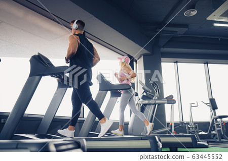 Music and exercises go together. Couple working exercise on treadmill. Focus is on man Music and exercises go together. Couple working exercise on treadmill. Focus is on man 63445552