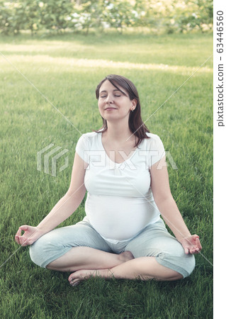 Young pregnant woman meditating while sitting in Young pregnant woman meditating while sitting in 63446560