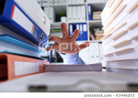 Among folders and documents mans hand seeks help 63446853