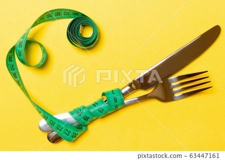 Crossed fork and knife are wrapped in measuring Crossed fork and knife are wrapped in measuring 63447161