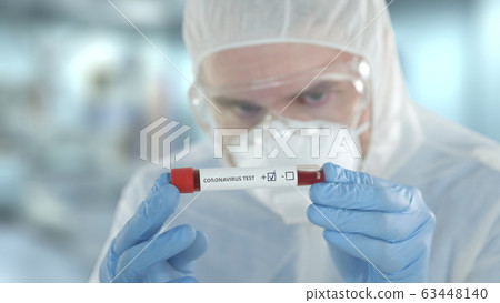 Unknown laboratory assistant wearing protection suit examines vial with positive coronavirus test Unknown laboratory assistant wearing protection suit examines vial with positive coronavirus test 63448140