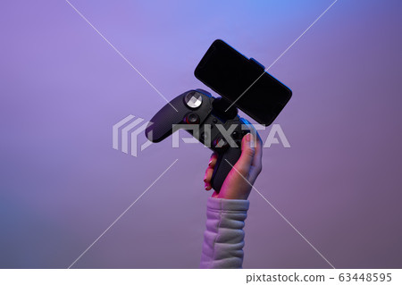 Female hands with a game joystick with smartphone on violet background. Female hands with a game joystick with smartphone on violet background. 63448595