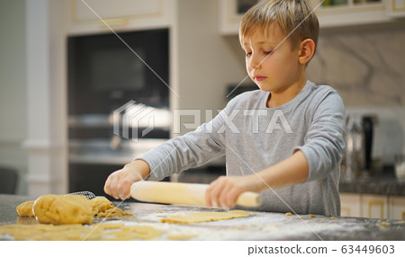 Child rolling dough with a rolling pin, close up Child rolling dough with a rolling pin, close up 63449603