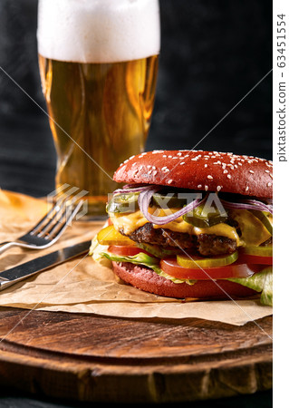 Delicious hot spicy black burger with chili pepper and glass of beer on cutting board on white wood table 63451554