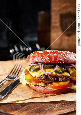 Fresh and juicy hamburger on a paper pillow with beer on a wooden table. Dark background, traditional american food. Junk food,... Fresh and juicy hamburger on a paper pillow with beer on a wooden table. Dark background, traditional american food. Junk food,... 63451555