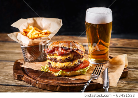 Delicious hot spicy black burger with chili pepper and glass of beer on cutting board on white wood table Delicious hot spicy black burger with chili pepper and glass of beer on cutting board on white wood table 63451558
