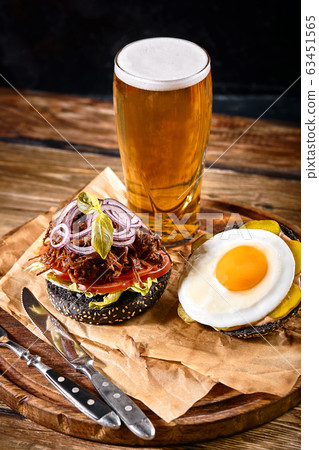 Delicious hot spicy black burger with chili pepper and glass of beer on cutting board on white wood table Delicious hot spicy black burger with chili pepper and glass of beer on cutting board on white wood table 63451565
