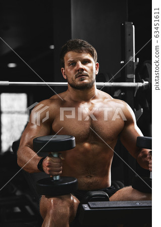 A shirtless muscular man is doing biceps exercises with dumbbell exercises as part of his bodybuilding workout. Fitness motivation, sports lifestyle, health, athletic body, body positive. Film grain A shirtless muscular man is doing biceps exercises with dumbbell exercises as part of his bodybuilding workout. Fitness motivation, sports lifestyle, health, athletic body, body positive. Film grain 63451611