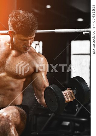 A shirtless muscular man is doing biceps exercises with dumbbell exercises as part of his bodybuilding workout. Fitness motivation, sports lifestyle, health, athletic body, body positive. Film grain A shirtless muscular man is doing biceps exercises with dumbbell exercises as part of his bodybuilding workout. Fitness motivation, sports lifestyle, health, athletic body, body positive. Film grain 63451612