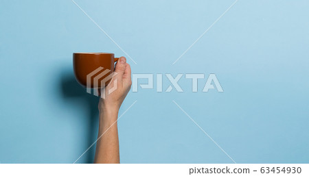 Woman holds in her hands a cup of coffee or tea drink blue bright background. Food drink concept. Copy space. 63454930
