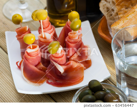 Traditional Spanish tapas - rolls of ham served with green olives 63456447