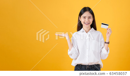 Attractive smiling Asian woman holding credit card payment on yellow background with copy space. Attractive smiling Asian woman holding credit card payment on yellow background with copy space. 63458037