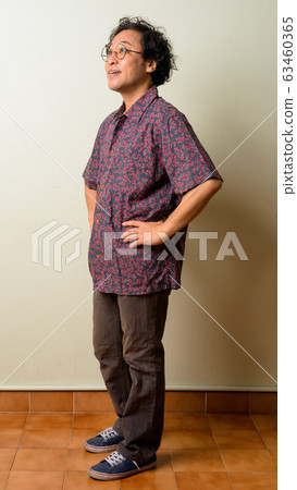 Full body shot of happy Japanese man with curly hair thinking Full body shot of happy Japanese man with curly hair thinking 63460365