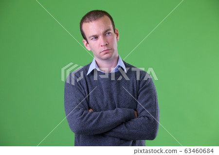 Portrait of businessman thinking with arms crossed against green background 63460684