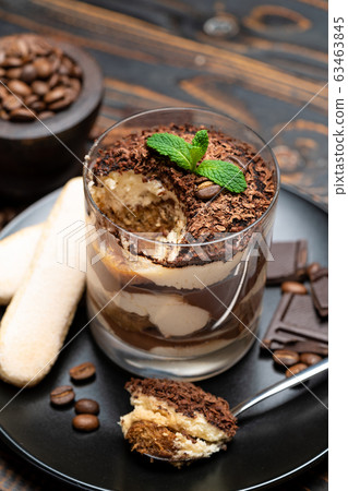 Classic tiramisu dessert in a glass cup, pieces of chocolate and savoiardi cookies on wooden background Classic tiramisu dessert in a glass cup, pieces of chocolate and savoiardi cookies on wooden background 63463845