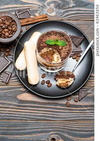 Classic tiramisu dessert in a glass cup, pieces of chocolate and savoiardi cookies on wooden background Classic tiramisu dessert in a glass cup, pieces of chocolate and savoiardi cookies on wooden background 63463850