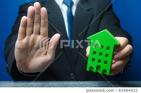 Man with a green house makes a stop gesture. Bank refusal to provide a mortgage loan. Housing problems, unscrupulous dishonest company builder. Confiscation pledged property. Refusal residence permit. Man with a green house makes a stop gesture. Bank refusal to provide a mortgage loan. Housing problems, unscrupulous dishonest company builder. Confiscation pledged property. Refusal residence permit. 63464832
