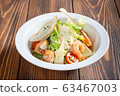 Plate of caesar salad with prawns on wooden table 63467003