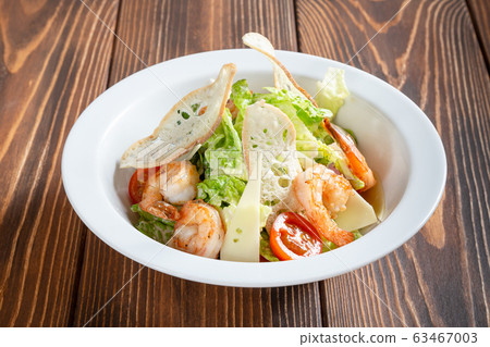 Plate of caesar salad with prawns on wooden table Plate of caesar salad with prawns on wooden table 63467003