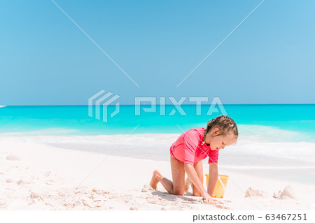 Little girl at tropical white beach making sand castle 63467251