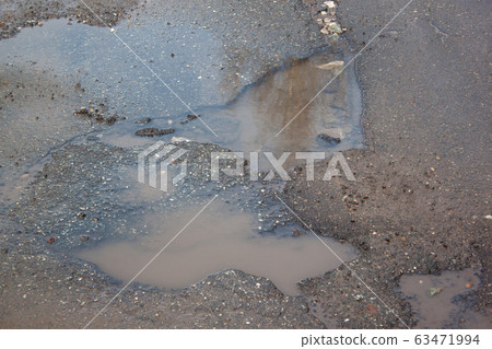 The bad asphalted road with a pothole with water. 63471994