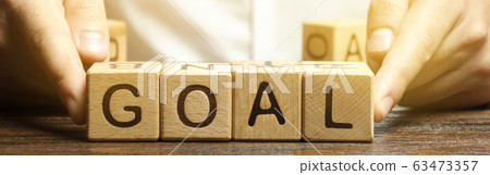 Businessman puts wooden blocks with the word Goal. The concept of achieving business goals. Reaching new heights. Execution of a business plan. Purposefulness. Perseverance. Target. Planning 63473357