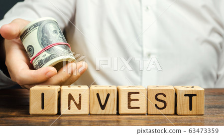 Wooden blocks with the word Invest and money in the hands of a businessman. Concept of investing in a business project. Economics and finance. Cash investments for profit 63473359