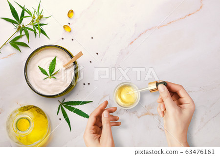 Pipette with CBD cosmetic oil in female hands on a table background with cosmetics, cream with cannabis and hemp leaves, marijuana Pipette with CBD cosmetic oil in female hands on a table background with cosmetics, cream with cannabis and hemp leaves, marijuana 63476161