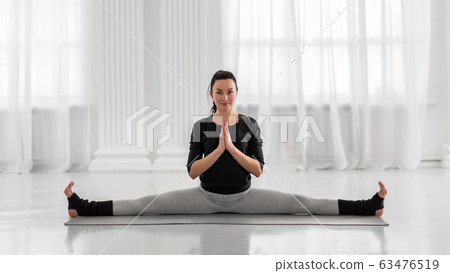 Young beautiful asian woman practicing yoga pose on gray mat. Samakonasana. Straight Angle Pose. Side Splits. 63476519