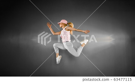 Young woman with fit body jumping and running against grey background. Female model in sportswear exercising Young woman with fit body jumping and running against grey background. Female model in sportswear exercising 63477115