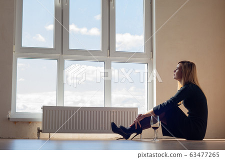 Sad girl sitting by the window in an empty 63477265