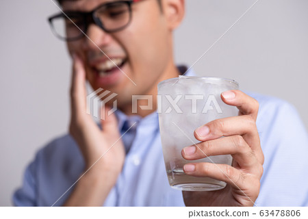 Young man with sensitive teeth and hand holding glass of cold water Young man with sensitive teeth and hand holding glass of cold water 63478806