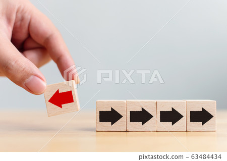Hand holding wooden block with red arrow facing the opposite direction black arrows 63484434